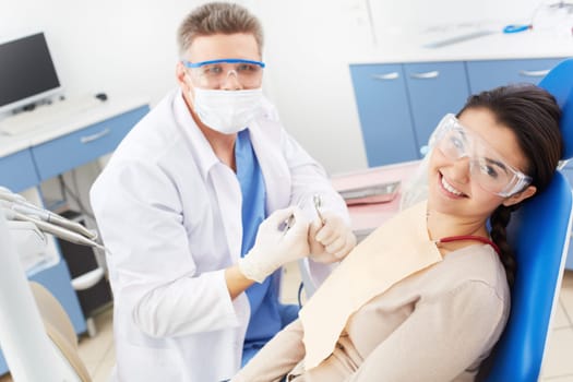 Happy girl in protective eyeglasses looking at camera with toothy smile at the dentist’s