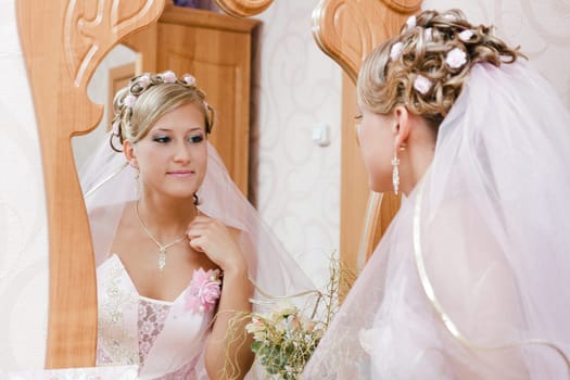 Beautiful bride in a pink dress looks in the mirror