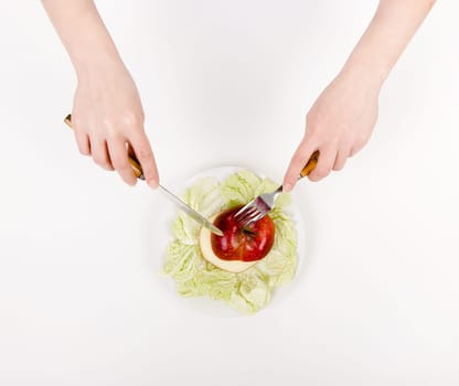 Women's hands with knife and fork on a plate with an apple