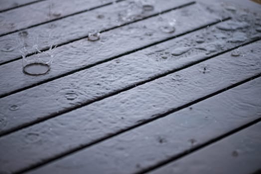 Splashing rain water droplets pattern on wooden table close-up