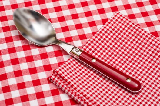 Spoon and napkin with checks in red and white on a tablecloth