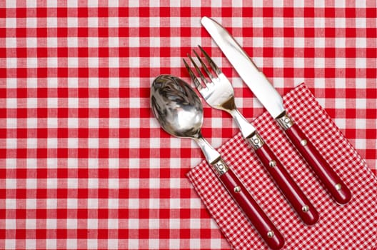 Cutlery made of red knife,fork and spoon on checkered napkin and tablecloth