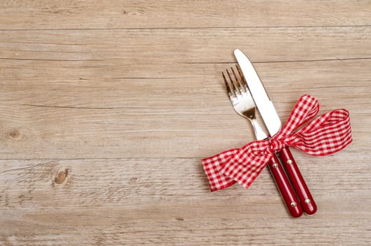 Rustic wooden table with knife and fork in red as a menu