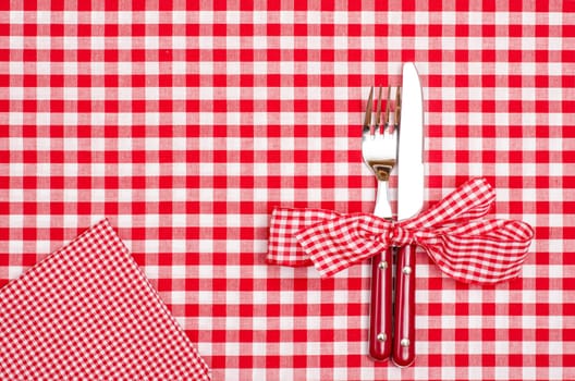 Knife and fork with bow and napkin on red checkered cloth from a dining table