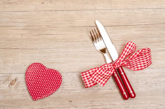 Knife and fork and red heart with white dots on a wooden table