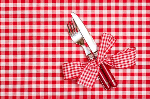 Knife and fork with red checkered bow on a tablecloth