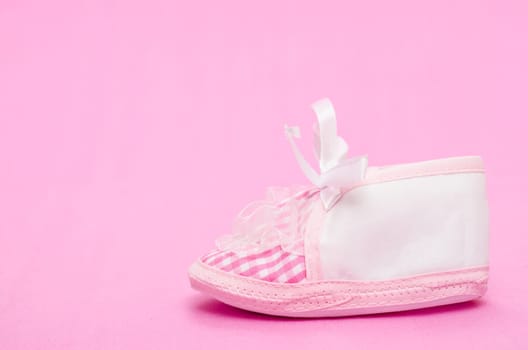 Female baby shoe with bow on pink background