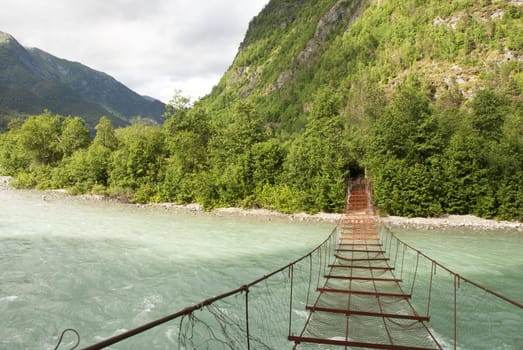 A Rusty Bridge Which Leads over a River into the Woods and to a huge Hill