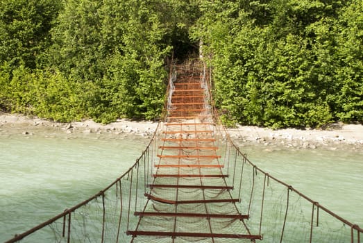 A Rusty Dangerous Bridge Leads over a Turquois River into the Woods