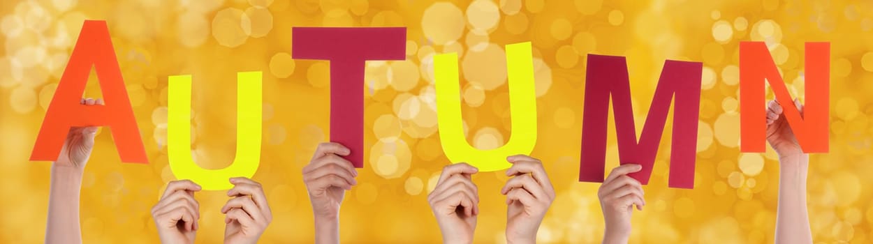 Many Hands Holding the Word Autumn with a Yellow Background