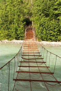 A Rusty Bridge Which Leads over a River into a Green Wall of Trees