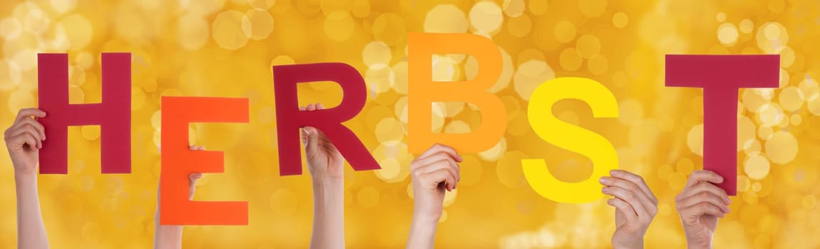 Many Hands Holding the German Word Herbst Which Means Fall or Autumn with a Yellow Background