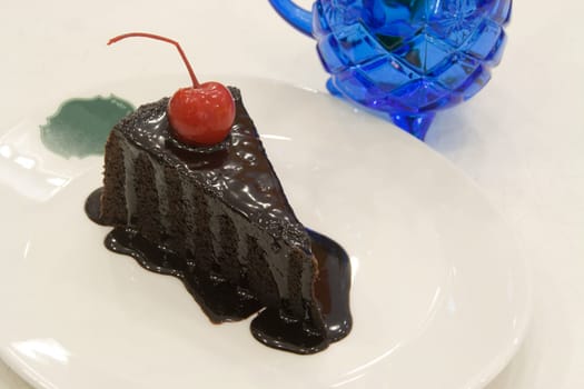 Chocolate cake decorated with red cherries on white plate.