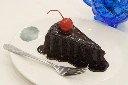 Chocolate cake decorated with red cherries on white plate.