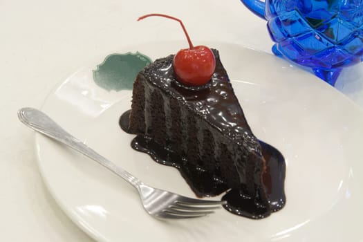 Chocolate cake decorated with red cherries on white plate.