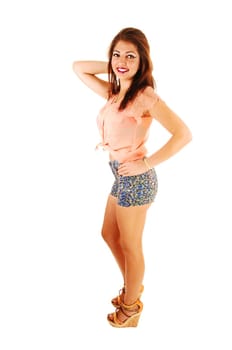 A young pretty woman standing in profile for white background in shorts.and heels, smiling and brunette hair..