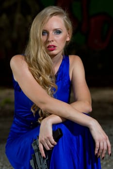 Sexy spy in blue cocktail dress holding gun, resting on the ground