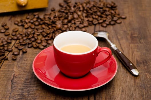 Red cup of espresso and a spoon in front of beans and coffee grinder