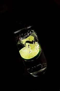 Lime falls into a glass of water against a black background