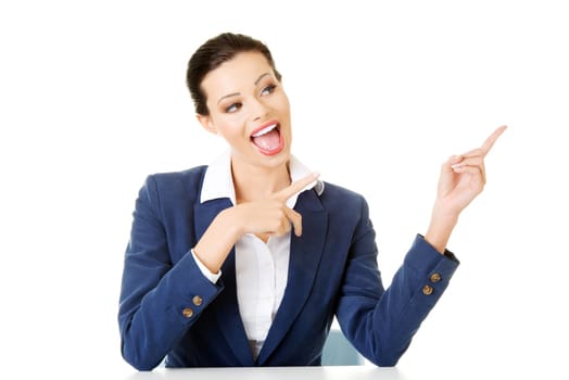 Business woman sitting at the desk and pointing with finger to empty copy space, isolated over white background