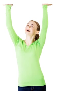 Smiling young woman is holding something abstract above her head. Happy girl with raised hands. Isolated on white background.