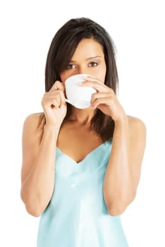 Attractive woman in nightwear drinking from cup, isoalted on white.