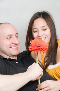 Upper body portrait of a young couple at home on the couch with flower in hand and amorous looks