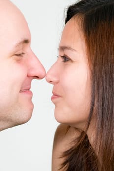 Head-and-shoulder shot in profile of a young couple nose to nose in front of a white background