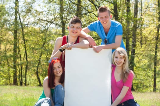 Four teenagers in colored shirts and a white board which can be used for your advertisements