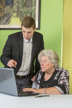 Elderly lady and young man working together on the laptop.