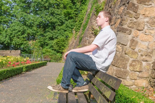 Young man sits on a bench and sunbathes