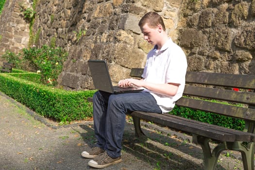 Young man sits on a bench and works with a laptop