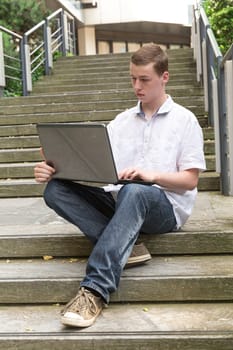Young man sits on stairs and works on his laptop