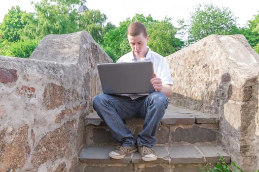 Young man sits on stairs and works on his laptop