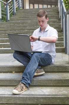 Young man sits on stairs and works on his laptop