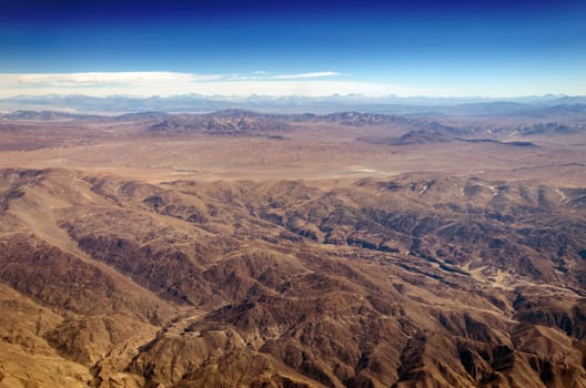 Dry desert and hills with snow capped mountains in the background somewhere over South America