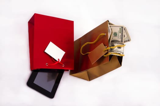 A red gift bag with a Tablet PC and a gold gift bag with dollars, isolated.