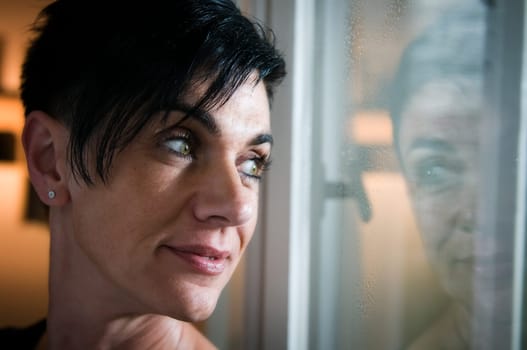 lateral and shady head proträt of a black-haired middle-aged woman looking thoughtfully smiling out of the window