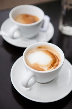 Closeup of two milk based coffees in white cups on cafe table