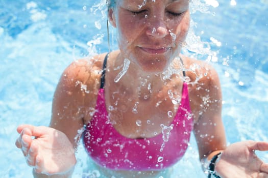 Happy female swimmer splashing water in face with eyes closed while in swimming pool