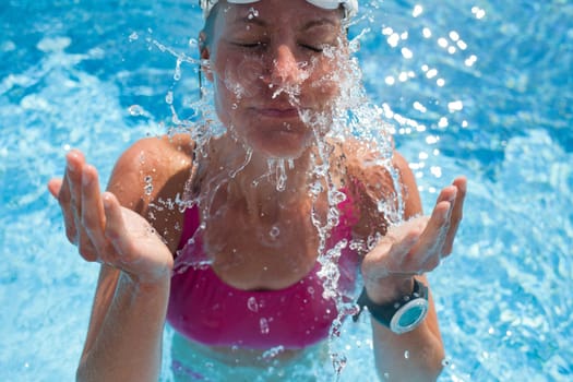 Happy female swimmer splashing water in face with eyes closed while in swimming pool