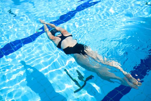 Female freediver diving underwater in outdoor swimming pool