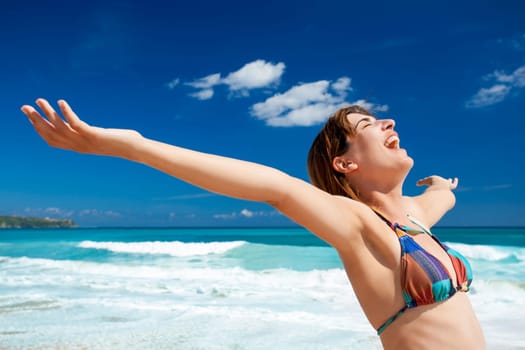 Beautiful young woman with arms open in a tropical beach enjoying the summer