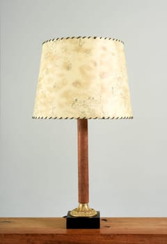 Classic table lamp with yellowish shade on wooden leg, close-up on the shelf against white background