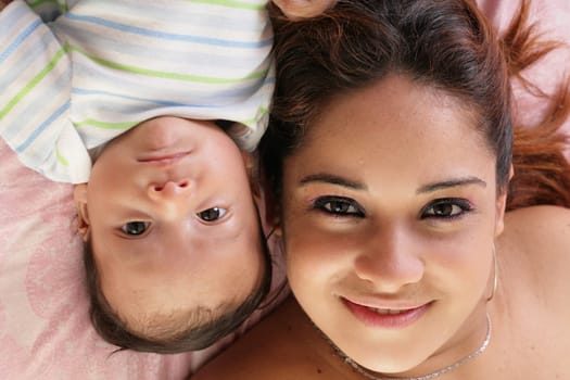 Portrait of a beautiful hispanic happy mother with baby lying down in bed