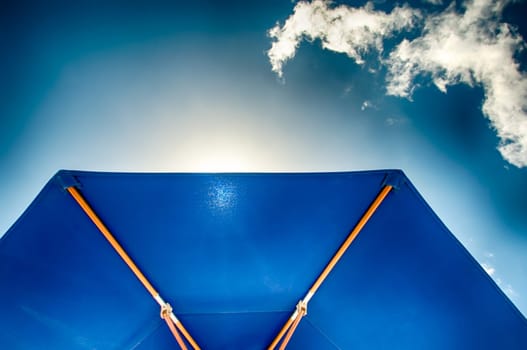 Part of a blue parasol backlit against a blue sky with clouds