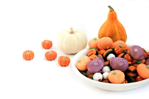 Dish full of halloween candy and two pumpkins on white background.