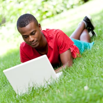 Young adult man student sitting in the meadow with notebook in the park Summer learning