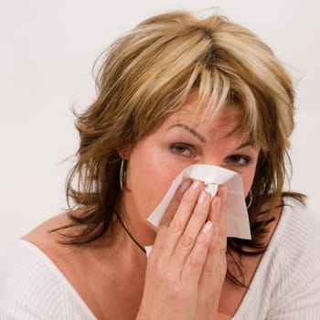 Head-and-shoulder shot of a middle-aged woman against a white background sniffing her nose