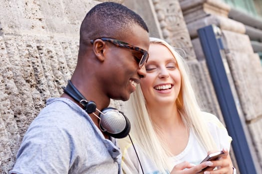 Laughing young friends in the city in summer with mobile phones